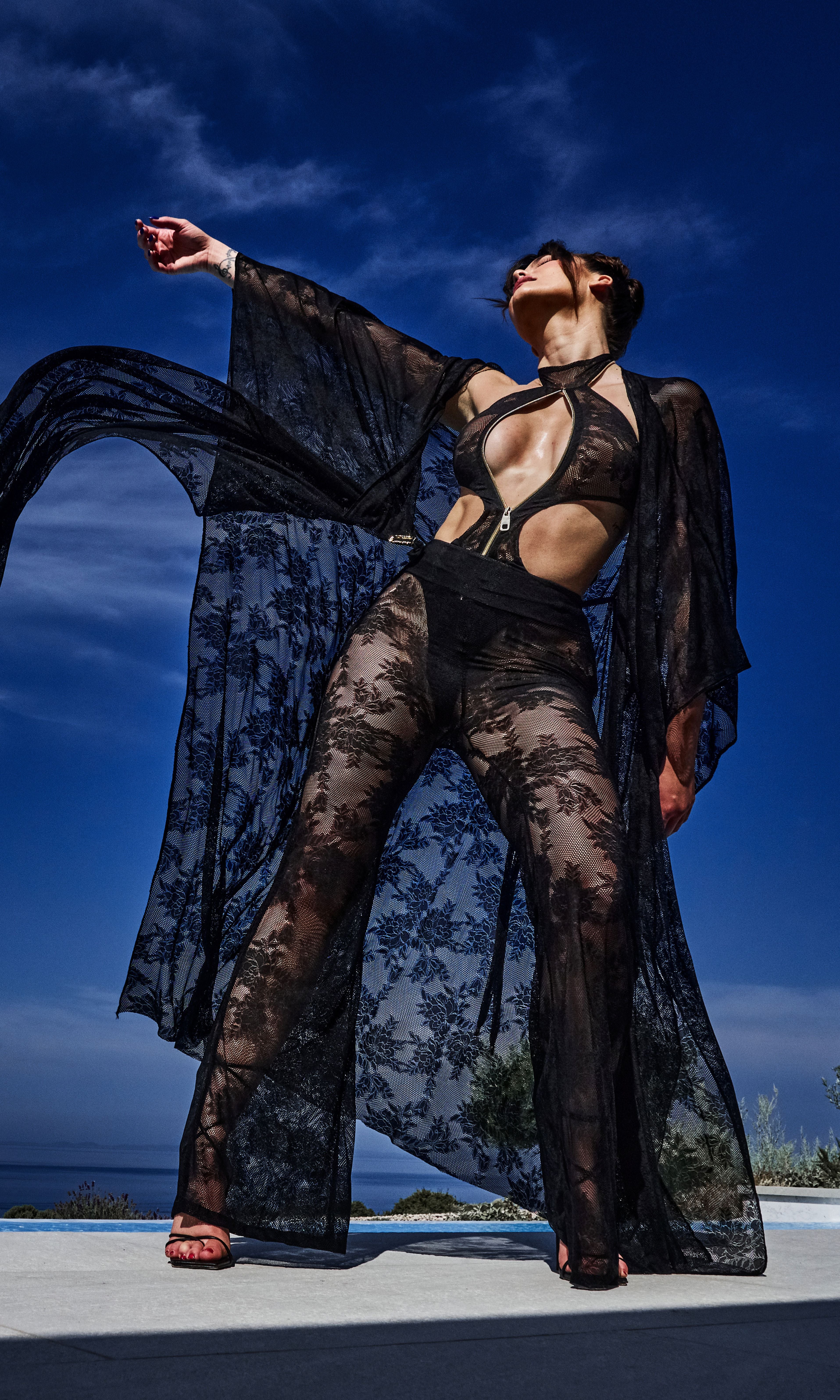 Model wearing Flora luxury sustainable sheer lace pants by Antoninias, designed with wide-leg silhouette and intricate floral detailing for premium resort wear and designer womenswear